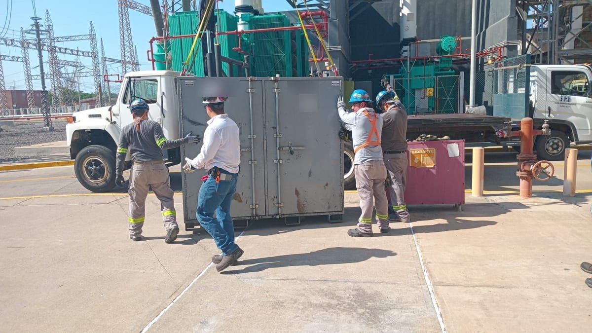 Cuadrilla con casco y arnés maniobrando un gabinete eléctrico descargado de un camión, frente a una subestación