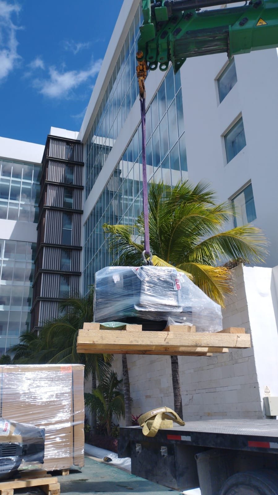 Pieza embalada y eslingada sobre polines, suspendida por la grúa tipo HIAB de RHT frente a un edificio en Cancún
