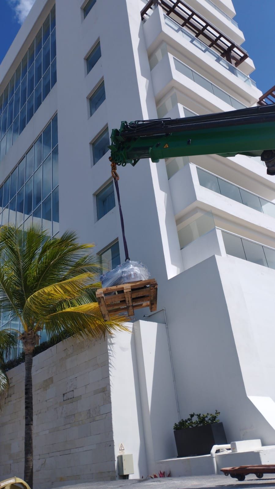 Grúa tipo HIAB de RHT izando una tarima embalada junto a la fachada de un edificio en Cancún
