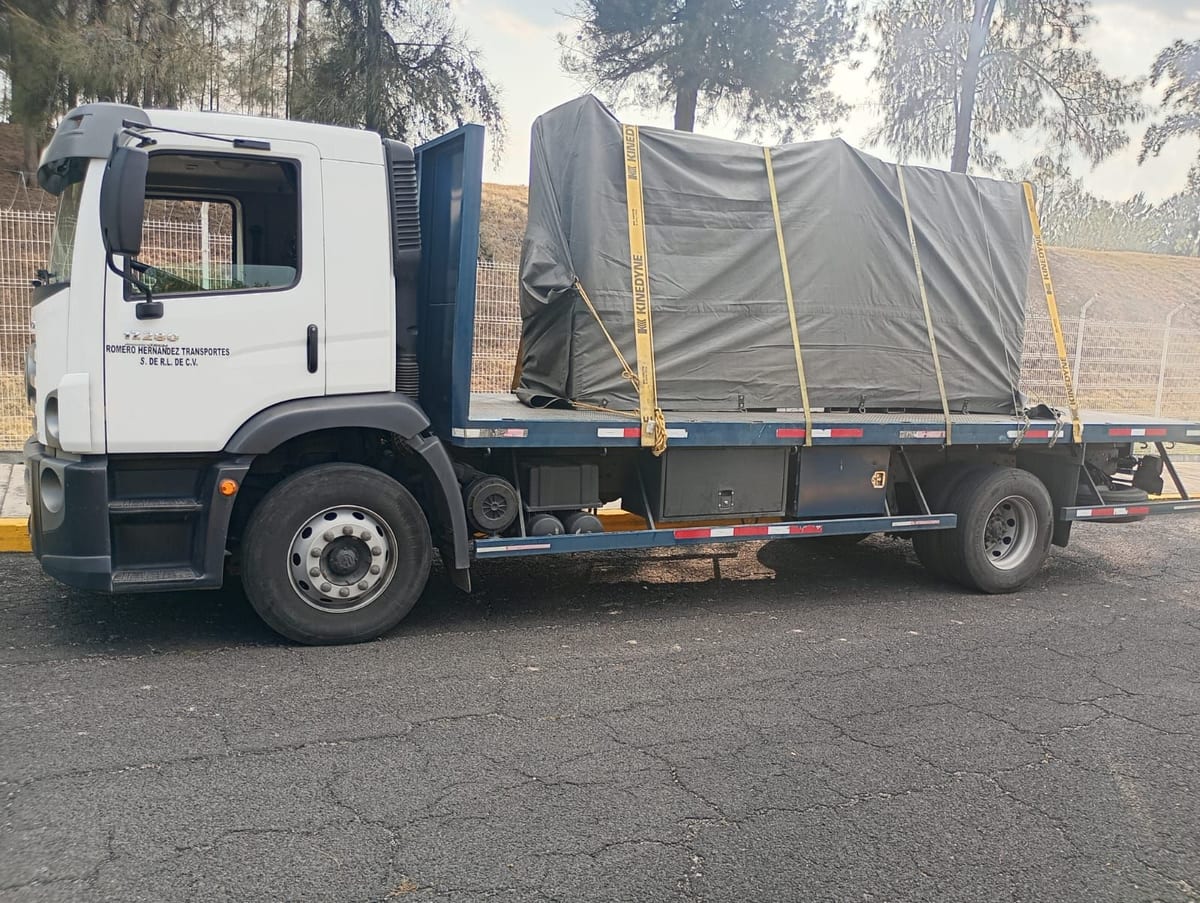 Camión de plataforma de RHT cargado con equipo entoldado y amarrado con cinchos, visto de costado